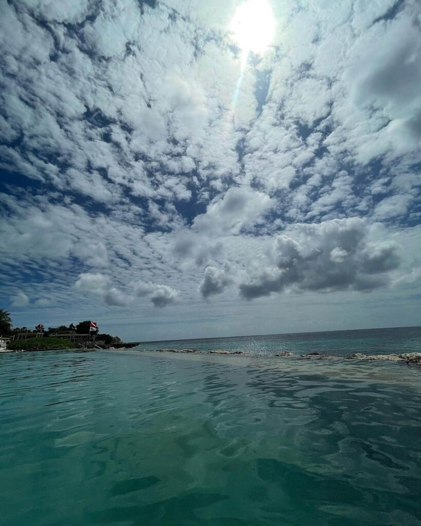 Vista panorámica de una playa paradisíaca con aguas turquesas y cielo parcialmente nublado, ideal para ilustrar consejos sobre qué llevar en la maleta de viaje para destinos tropicales.