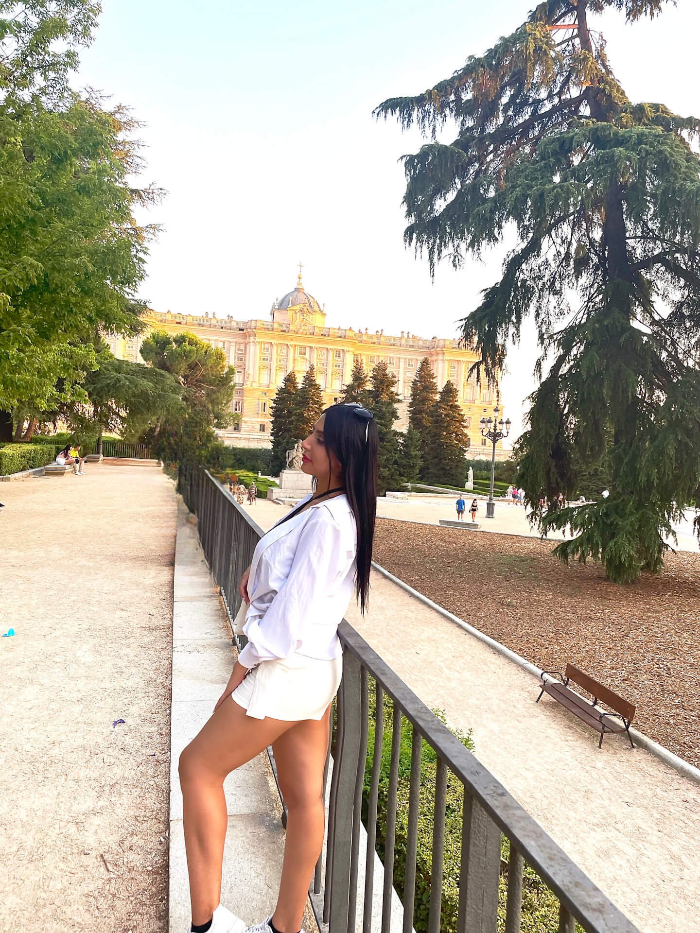 mujer en un parque con vista al Palacio Real de Madrid al fondo, rodeada de naturaleza y arquitectura histórica