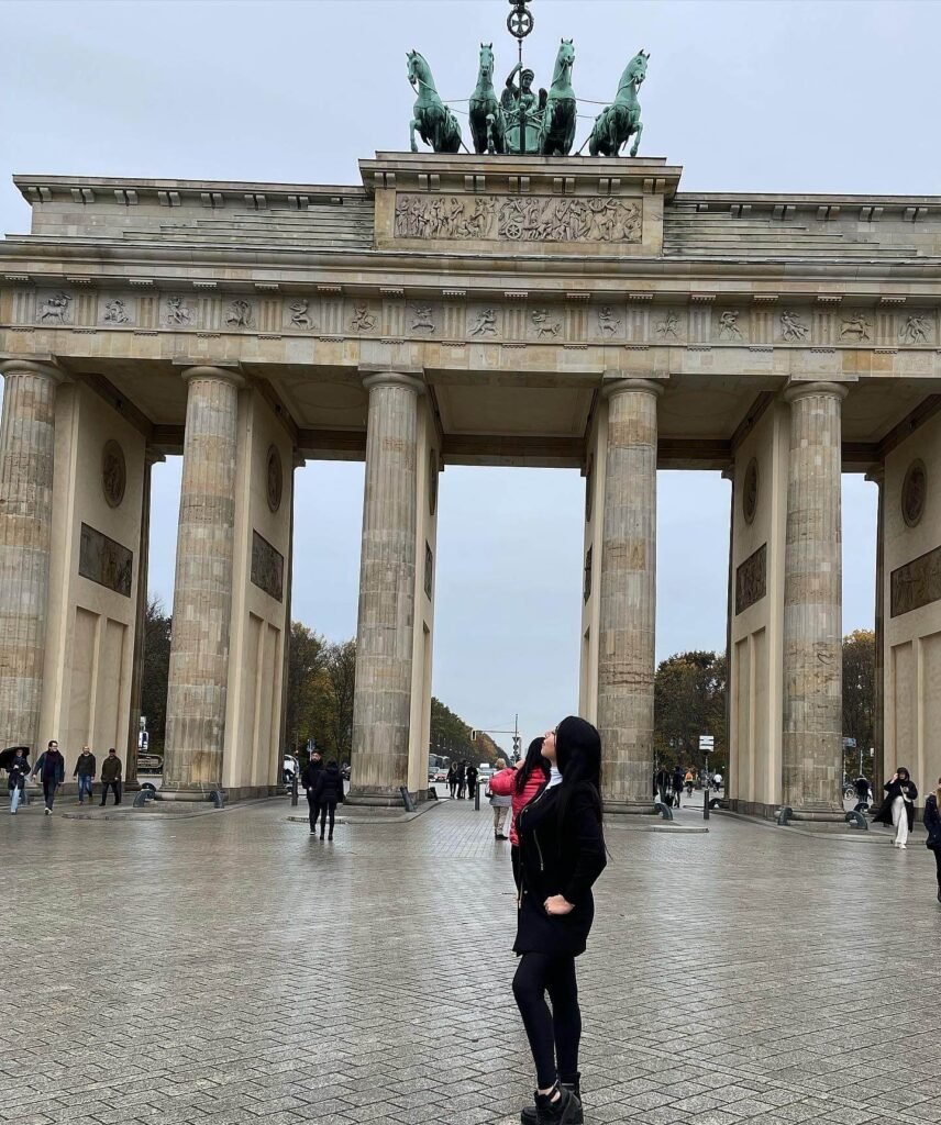 Mujer admirando la icónica Puerta de Brandeburgo en Berlín durante un día nublado, uno de los monumentos más emblemáticos de Alemania.