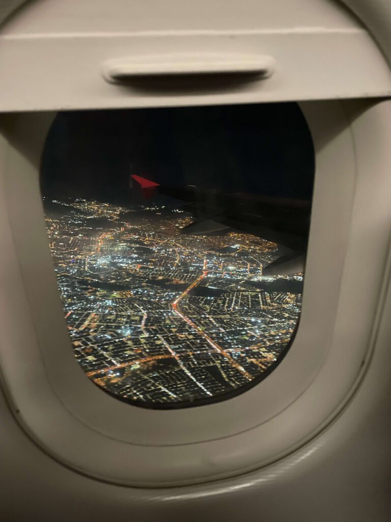 Fotografía desde la ventana de un avión mostrando una ciudad iluminada de noche, ideal para representar el comienzo de un viaje o aventura.
