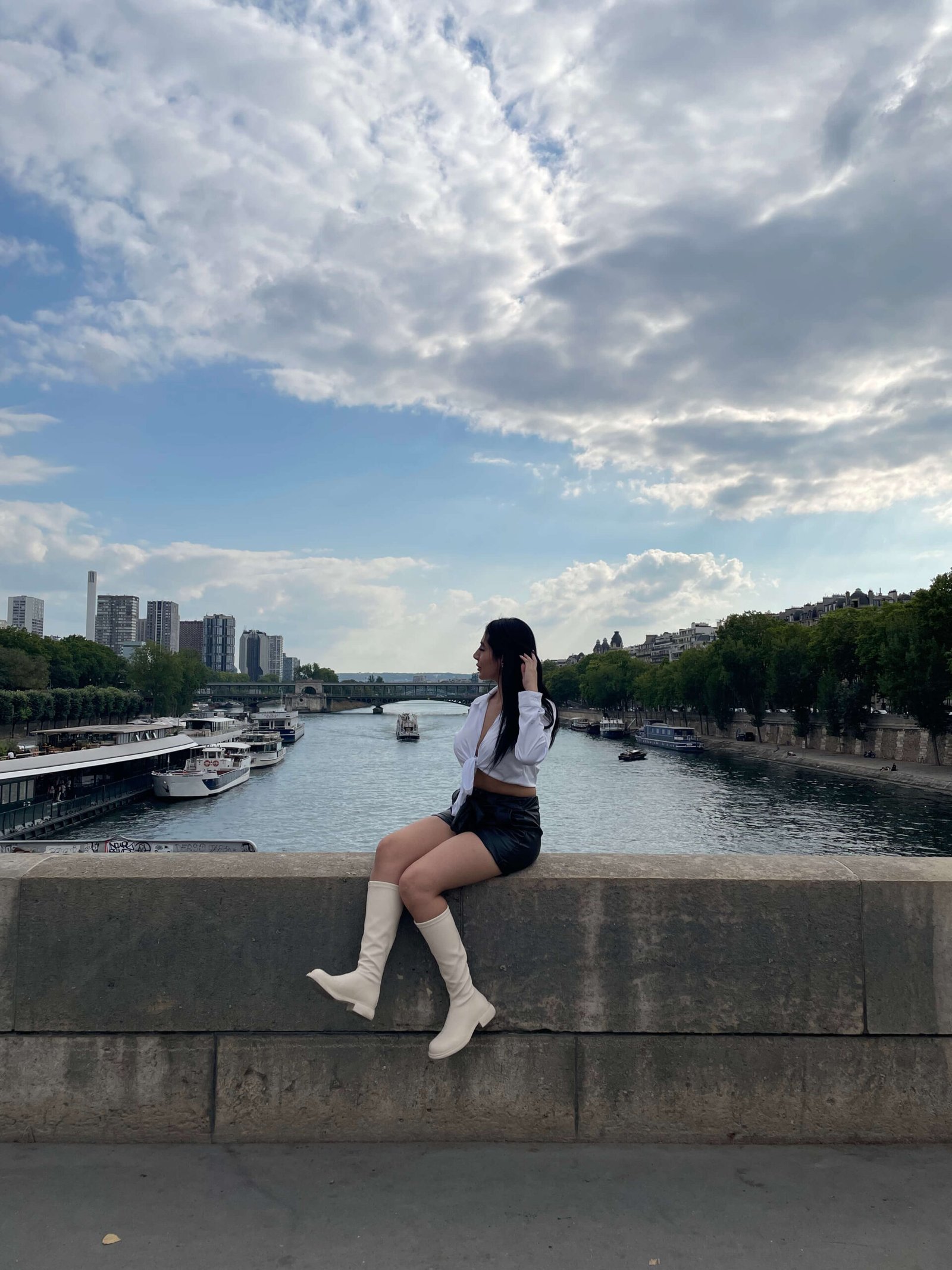 Viajera sentada en un puente con vista al río Sena en París, disfrutando del paisaje urbano; imagen representativa de planificación inteligente de viajes con apps móviles.